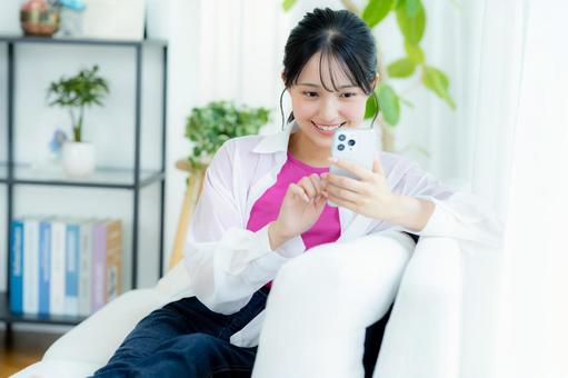 部屋でスマホを操作する若い女性 部屋でスマホを操作する若い女性 スマホ,笑顔,女性の写真素材