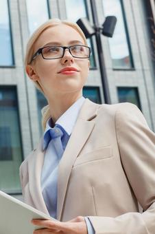 オフィスビルの外でタブレットを持って立つメガネを掛けた外国人女性 ビジネスウーマン,ビジネス,女性の写真素材