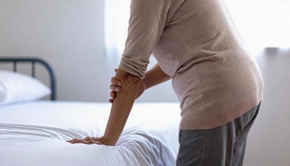 慎重にベッドから降りる高齢女性患者 慎重にベッドから降りる高齢女性患者の写真
