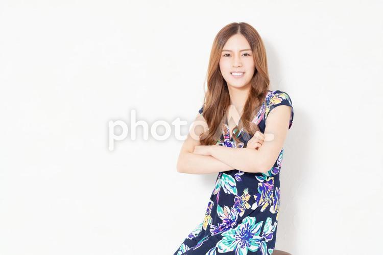 白い壁の前で腕を組んでいる、青いワンピースを着た若い女性 女性,笑う,ポーズの写真素材