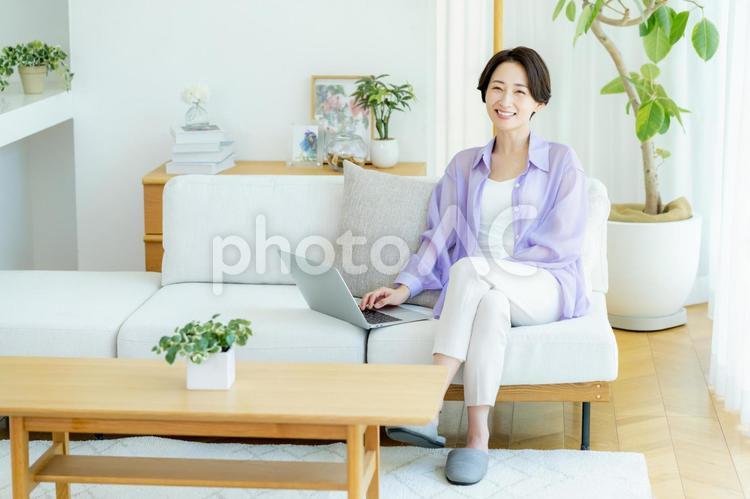 部屋でノートパソコンを使うミドル女性 女性,笑顔,テーブルの写真素材