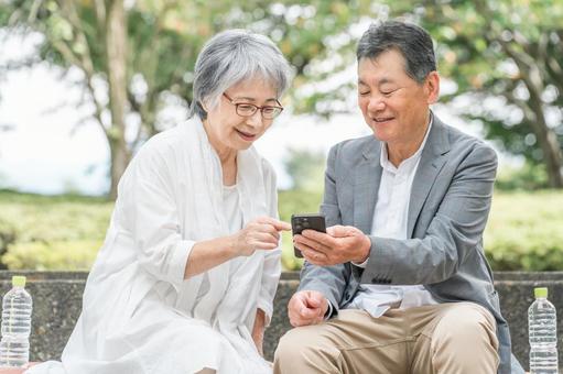 公園でスマホを見ながら会話する高齢者夫婦 シニア,スマホ,アプリの写真素材