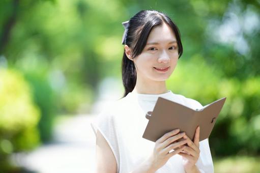 屋外で白いノースリーブワンピースの女性が読書するの写真