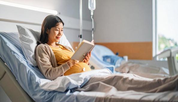 本を読んで安静にして点滴を打つ妊婦の写真