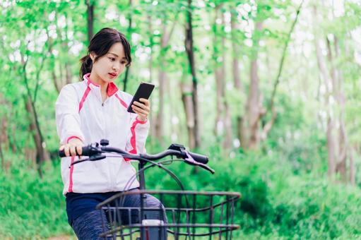 自転車に乗りながらスマホを使う女性 自転車に乗りながらスマホを使う女性の写真