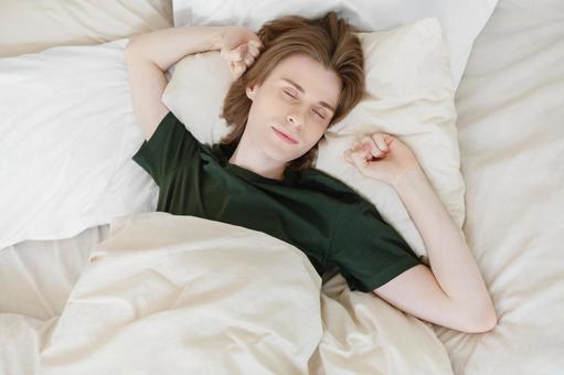 両手を上げてベッドで寝ている若い男性 男性,外国人,欧米人の写真素材