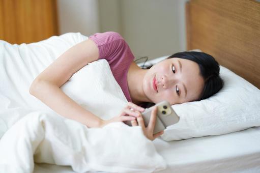 布団に入りスマホを見ている女性 女性,スマートフォン,持つの写真素材