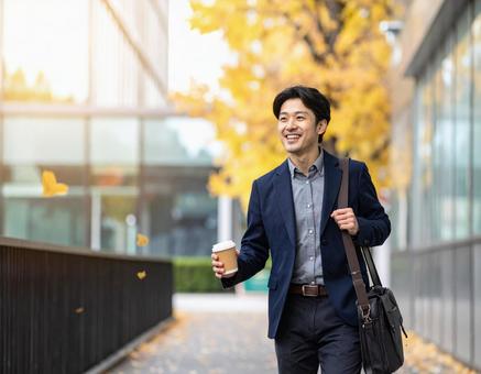 オフィス街を笑顔で歩く通勤中の男性 オフィス街を笑顔で歩く通勤中の男性の写真