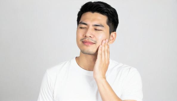 頬を触る白いTシャツの男性モデル 頬を触る白いTシャツの男性モデルの写真