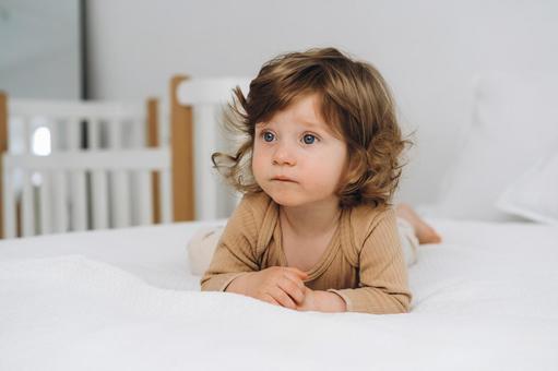 ベッドに寝転ぶベージュの服の子供 ベッドに寝転ぶベージュの服の子供 赤ちゃん,かわいい,寝転ぶの写真素材
