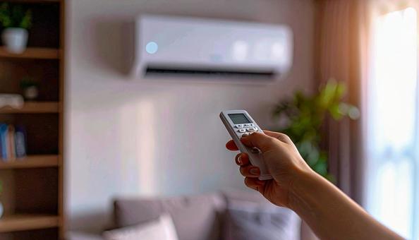 エアコンを操作するリモコンを持つ女性の手の写真