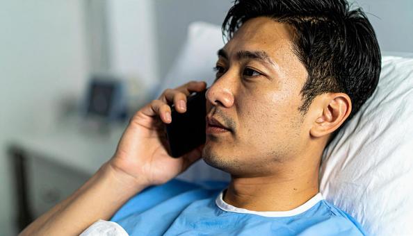 病室のベッドから携帯で話をする男性患者 病室のベッドから携帯で話をする男性患者の写真