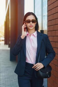 オフィスビルの外でスマートフォンで電話しているサングラスを掛けたビジネスウーマン ビジネスウーマン,ビジネス,女性の写真素材