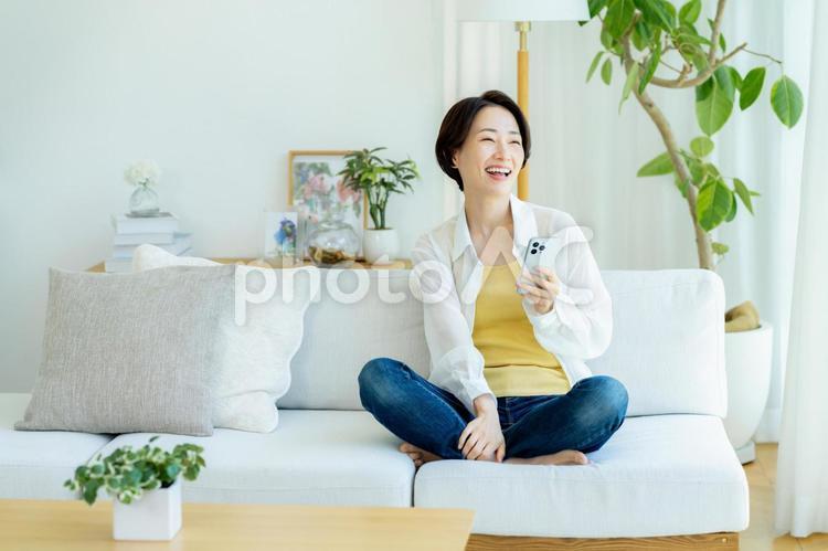 部屋でスマホを操作するミドル女性 スマホ,笑顔,女性の写真素材