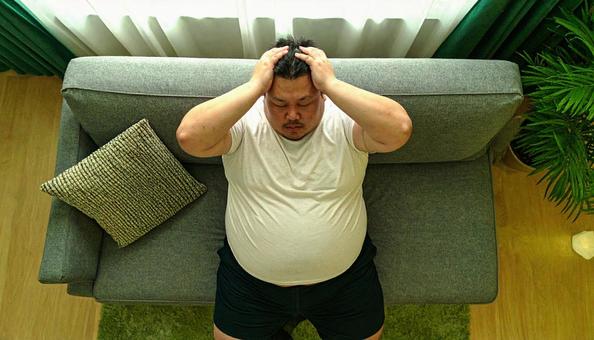 肥満で疲れやすく、額に手をやる男性 肥満で疲れやすく、額に手をやる男性の写真