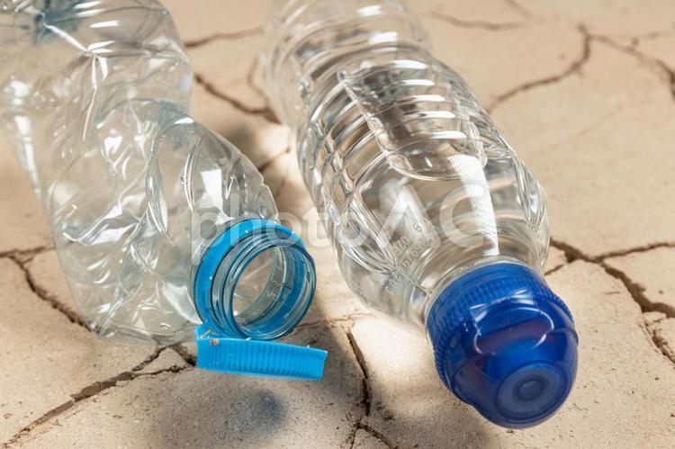 ひび割れた土の地面の上のペットボトルゴミと水の入ったペットボトル 温暖化,水不足,乾燥の写真素材