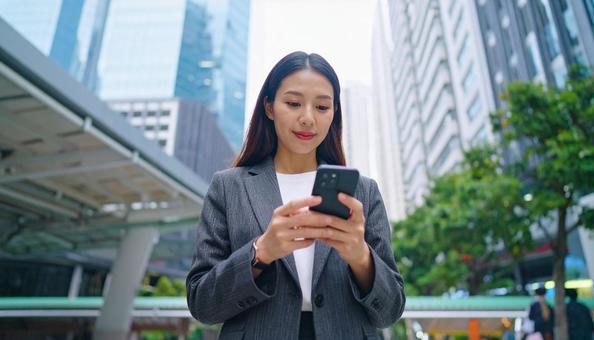 オフィス街でスマホ操作をする日本人女性 オフィス街でスマホ操作をする日本人女性の写真