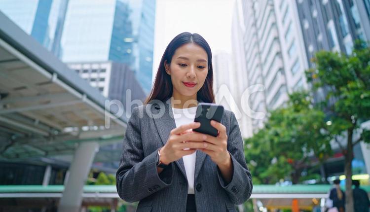 オフィス街でスマホ操作をする日本人女性 キャリアウーマン,ビジネスウーマン,スマートフォンの写真素材