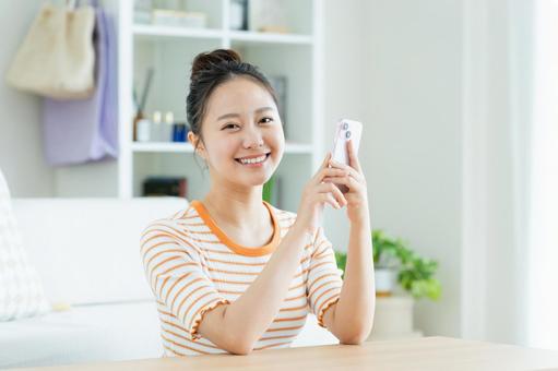 リビングでスマホを使う若い女性 リビングでスマホを使う若い女性の写真
