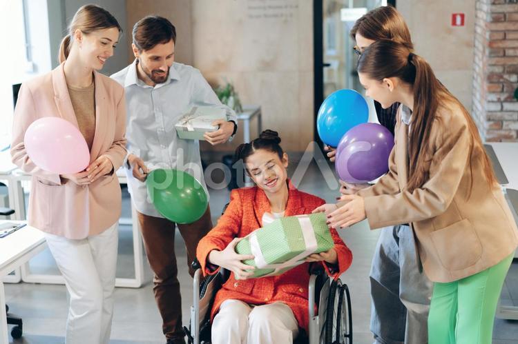 オフィスで誕生日プレゼントをもらった車椅子に乗った女性 ビジネス,ビジネスマン,ビジネスウーマンの写真素材