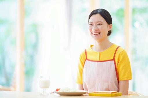 料理を前に笑うエプロンの女性の写真