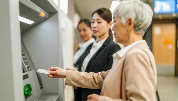 ATMでお金を引き出す老女と心配顔銀行員 ATMでお金を引き出す老女と心配顔銀行員の写真