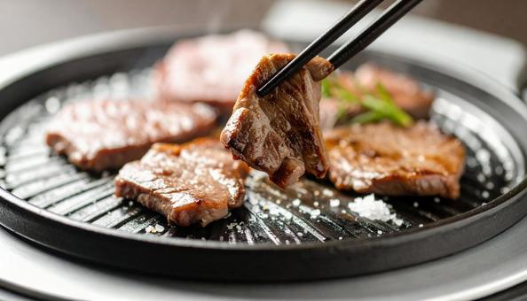 焼肉を鉄板で焼いて鉄箸ですくう 焼肉を鉄板で焼いて鉄箸ですくうの写真