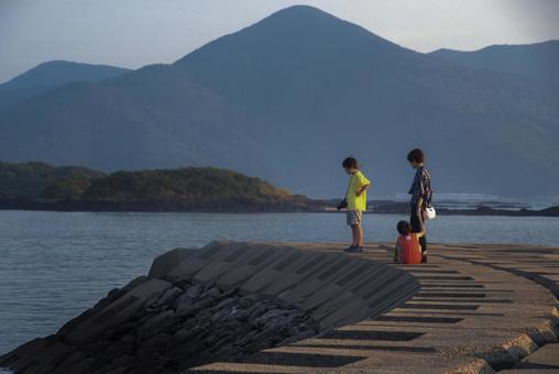 <素材>堤防から夕暮れの海を眺める親子 <素材>堤防から夕暮れの海を眺める親子の写真
