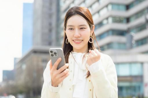 ビル街でスマホを見て喜ぶ女性 ビル街でスマホを見て喜ぶ女性 スマホ,ガッツポーズ,元気の写真素材