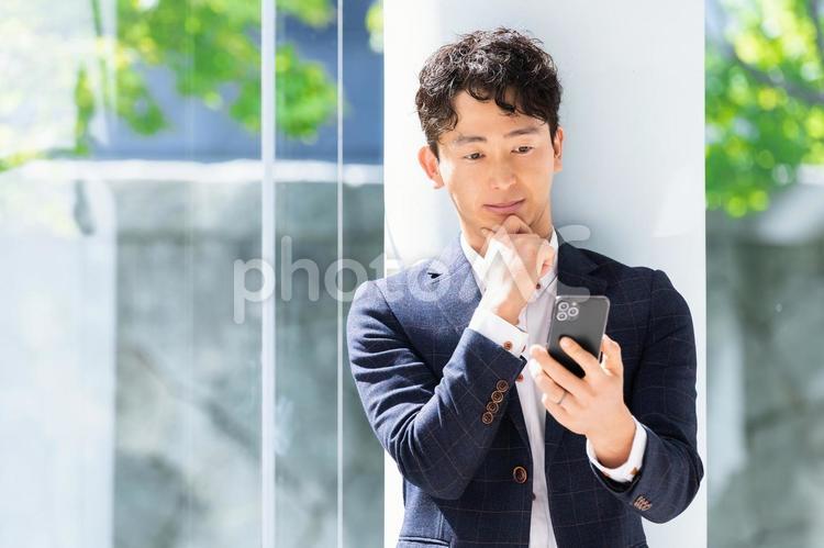 スマホの画面を見て考える男性ビジネスマン 男性,スマホ,ビジネスの写真素材