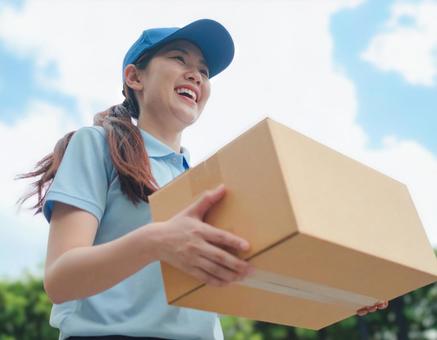 笑顔で荷物を届ける配達員の女性 笑顔で荷物を届ける配達員の女性の写真
