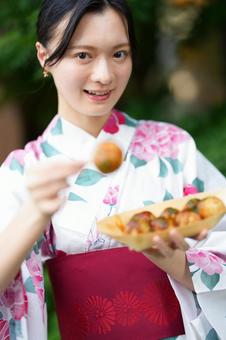 浴衣姿の女性が笑顔で食べ物を見せる 女性,浴衣,たこ焼きの写真素材