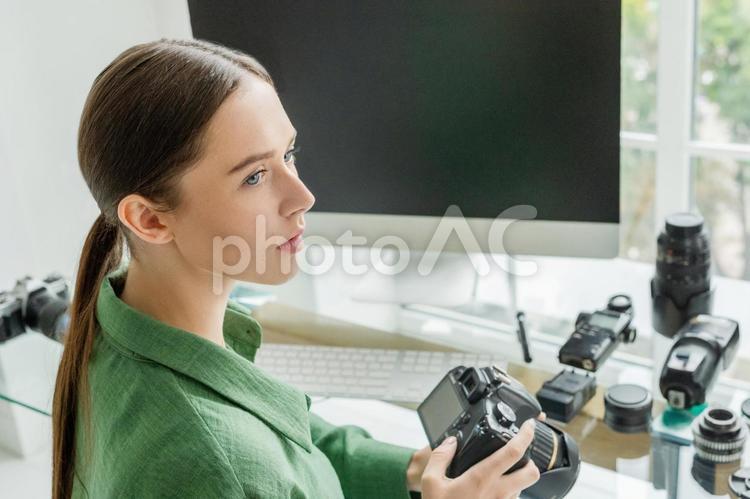 仕事部屋でカメラを持って横を向いて考えている女性写真家 フォトグラファー,カメラマン,写真家の写真素材