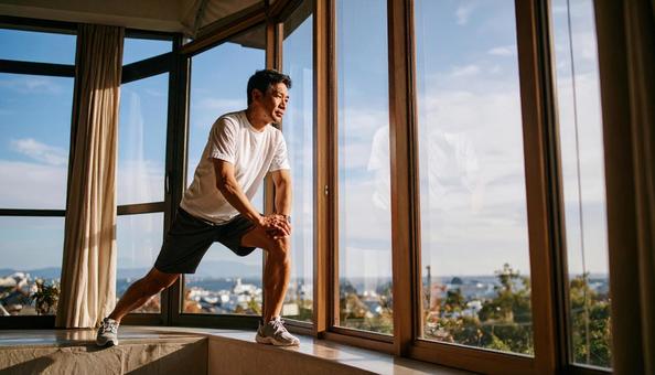 窓際で、ストレッチをするシニア男性 窓際で、ストレッチをするシニア男性の写真
