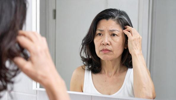 鏡の前で抜け毛を確認する中年女性 鏡の前で抜け毛を確認する中年女性の写真