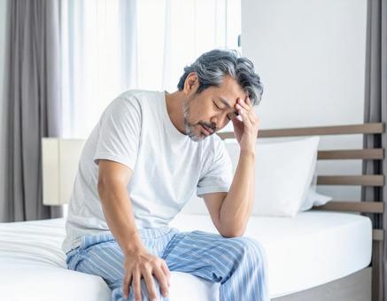 寝起きで座って頭を抱えるパジャマ姿の男性 寝起きで座って頭を抱えるパジャマ姿の男性の写真