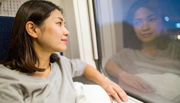 夜、電車内から外を見る日本人女性の写真