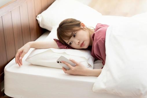 寝ながらスマホを使う女性 寝ながらスマホを使う女性 女性,人物,スマートフォンの写真素材