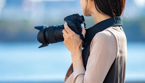 一眼レフを首から下げ手に取る女性の写真