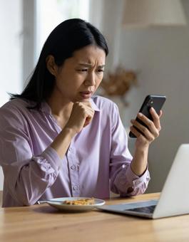 スマホを見て不安そうな女性(室内) スマホを見て不安そうな女性(室内)の写真