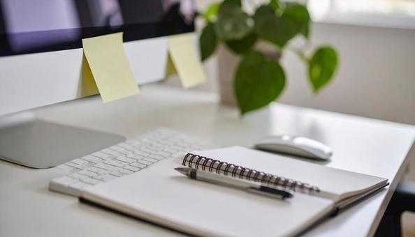 付箋がついたノートとパソコンデスクの写真