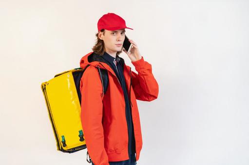 配達バッグを背負って電話している男性（白背景） 配達,フードデリバリー,デリバリーの写真素材