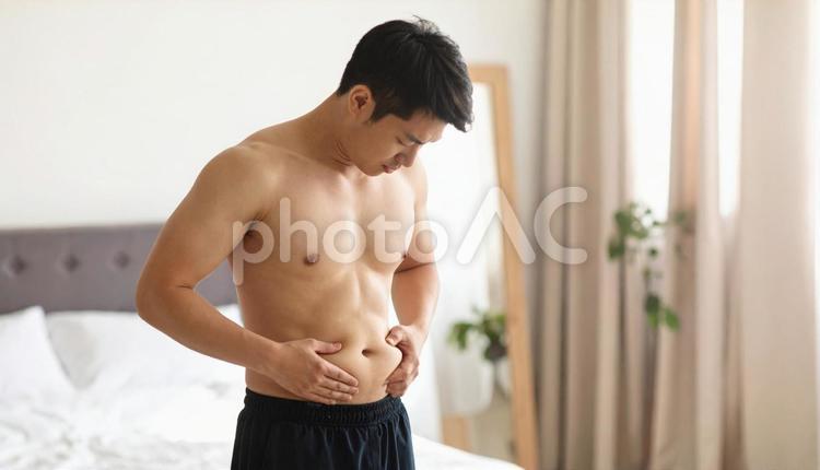 室内で自分のお腹の脂肪を気にする若い男性 人物,男性,ダイエットの写真素材