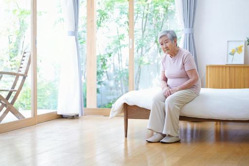 窓際のベッドで心配そうな顔のおばあちゃん 女性,ベッド,座るの写真素材
