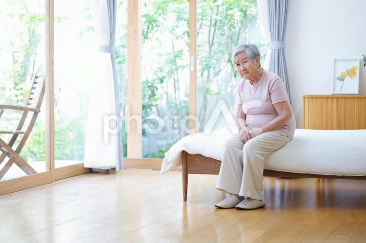 窓際のベッドで心配そうな顔のおばあちゃん 女性,ベッド,座るの写真素材