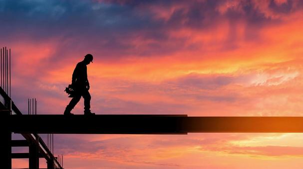 夕焼けに立つ建設作業員 夕焼けに立つ建設作業員の写真