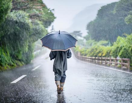 雨の日に傘をさして道路を歩く男性 雨の日に傘をさして道路を歩く男性の写真
