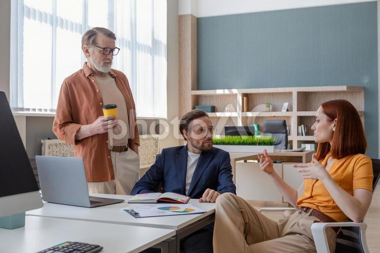デスクで話をしている3人のビジネスパーソン ビジネスマン,ビジネスウーマン,男性の写真素材