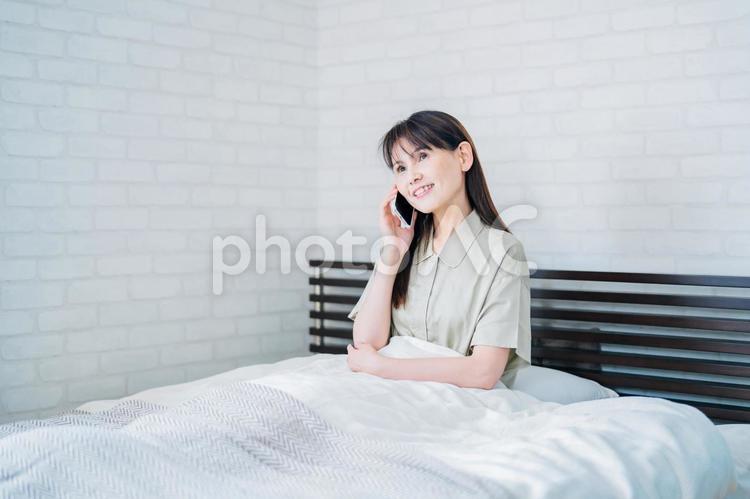 ベッドでスマホを使うミドル世代の女性（通話・笑顔） スマホ,通話,スマートフォンの写真素材