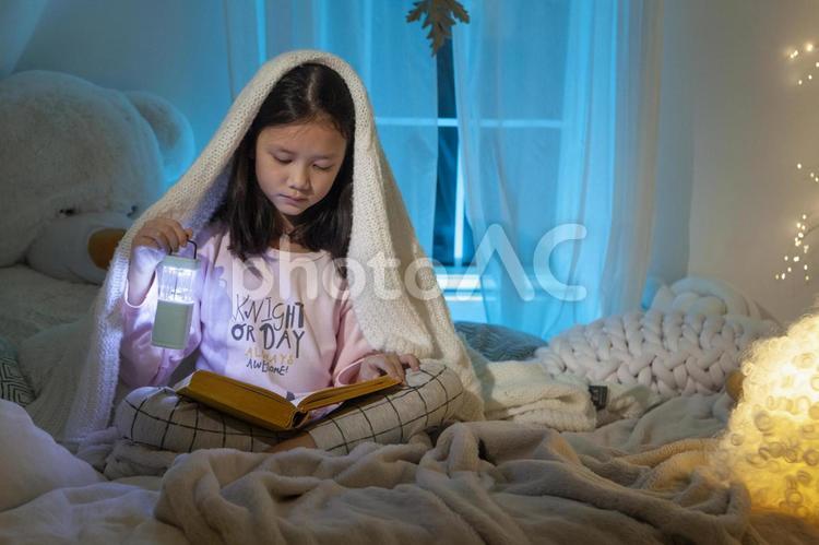 ベッドに座って毛布を被り本を読んでいる女の子 子ども,女の子,外国人の写真素材